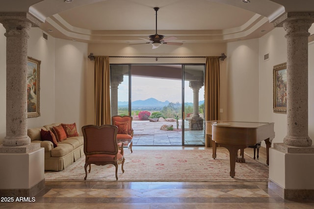 interior space with a tray ceiling, a mountain view, a ceiling fan, and ornate columns