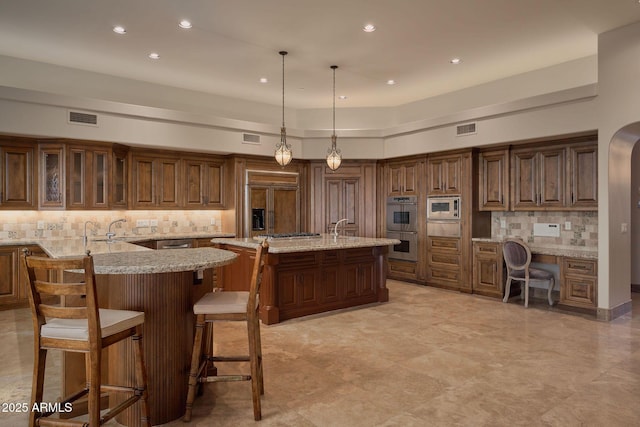 kitchen featuring a breakfast bar, a center island with sink, visible vents, built in appliances, and backsplash