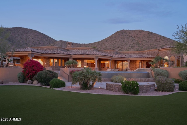 back of property featuring a tile roof, a mountain view, and a lawn