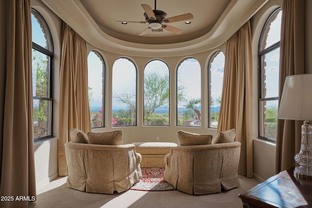 living area with carpet, a ceiling fan, and a raised ceiling
