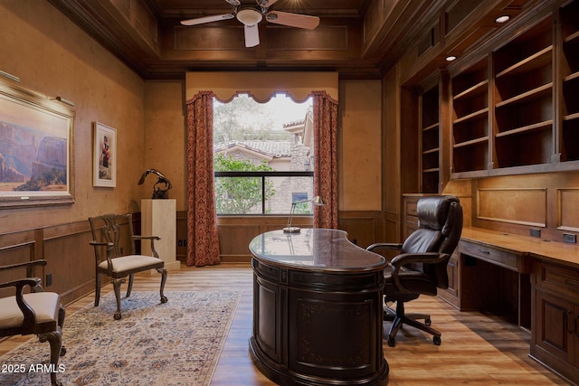 office area featuring a ceiling fan, ornamental molding, light wood-style flooring, and a wainscoted wall