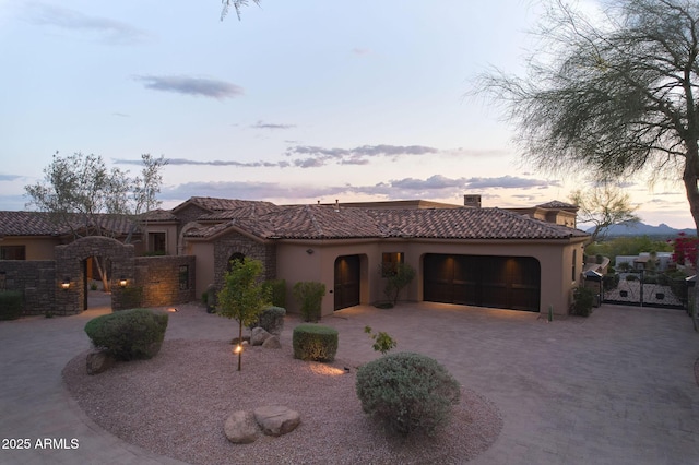 mediterranean / spanish-style house with decorative driveway, an attached garage, stucco siding, a tile roof, and a gate