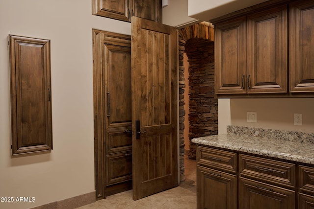 kitchen featuring dark brown cabinets and light stone countertops