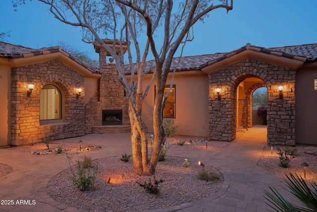 exterior space with stone siding, a patio, stucco siding, a tile roof, and an outdoor stone fireplace