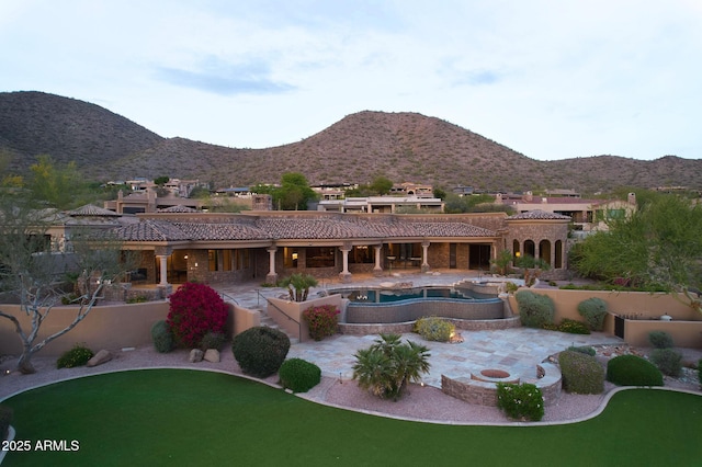 rear view of property featuring an in ground hot tub, a patio, a tiled roof, and a mountain view