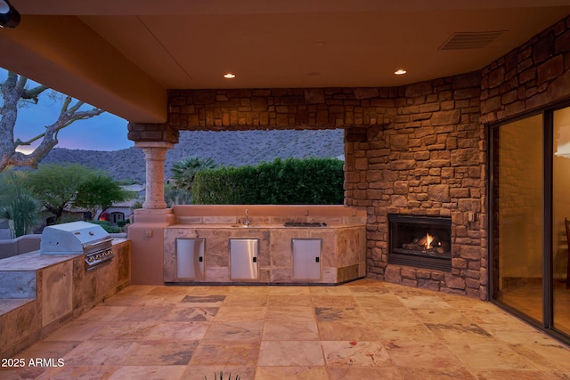 view of patio with a sink, area for grilling, an outdoor stone fireplace, visible vents, and grilling area