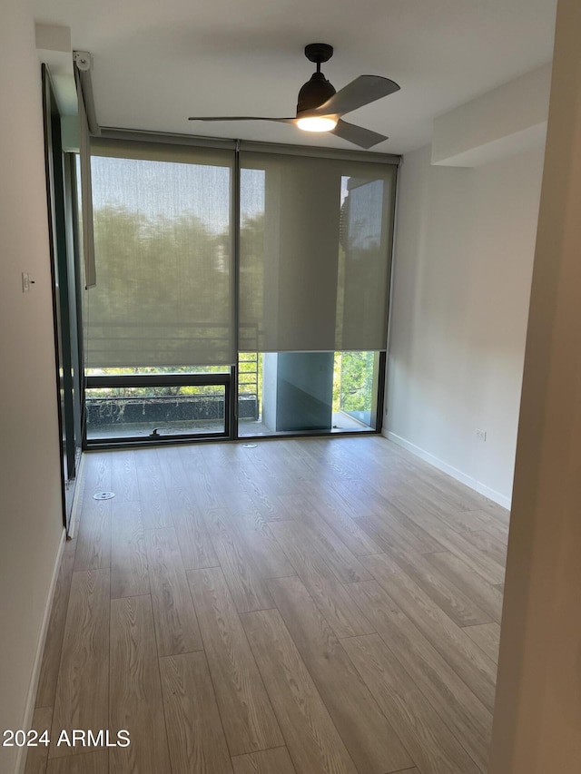 unfurnished room with ceiling fan, a wall of windows, baseboards, and wood finished floors