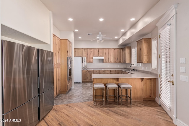 kitchen with white refrigerator, a kitchen bar, stainless steel refrigerator, kitchen peninsula, and light hardwood / wood-style flooring