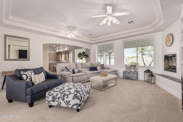 carpeted living room with ceiling fan and a tray ceiling