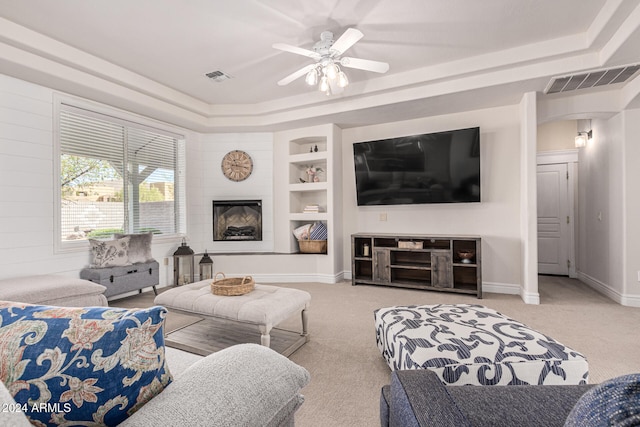 carpeted living room featuring built in shelves, a tray ceiling, and ceiling fan