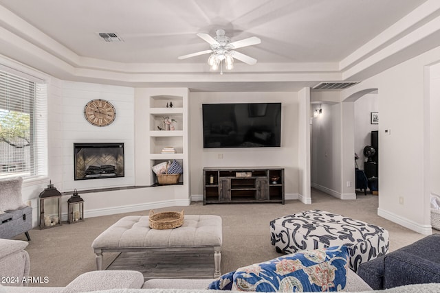 living room with built in features, a tray ceiling, light carpet, and ceiling fan