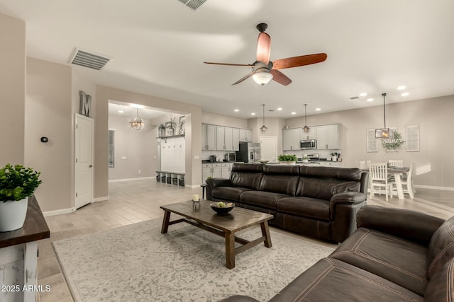 living room with ceiling fan with notable chandelier and light hardwood / wood-style floors