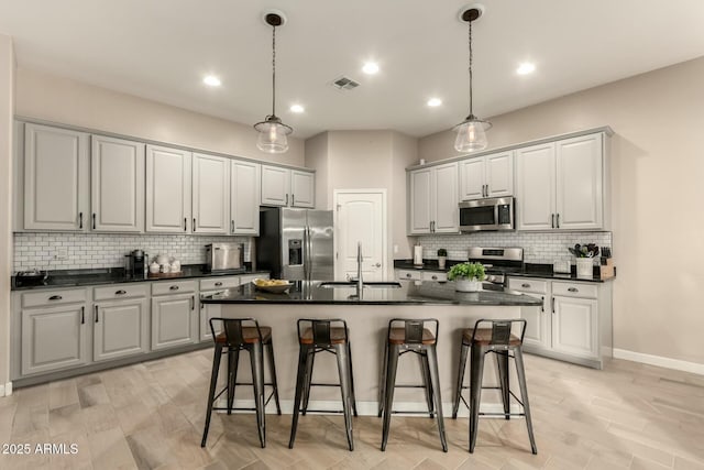 kitchen with sink, hanging light fixtures, stainless steel appliances, a kitchen breakfast bar, and a center island with sink