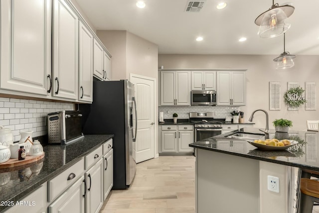 kitchen featuring sink, decorative light fixtures, dark stone countertops, appliances with stainless steel finishes, and white cabinets