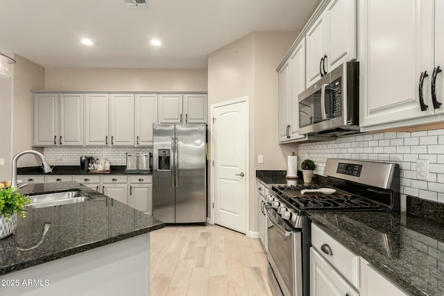 kitchen featuring sink, dark stone countertops, white cabinets, stainless steel appliances, and light hardwood / wood-style flooring