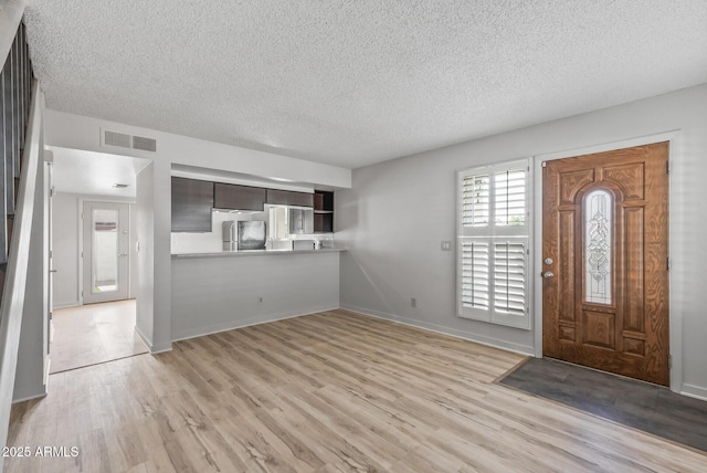 foyer entrance with visible vents, light wood finished floors, and a textured ceiling