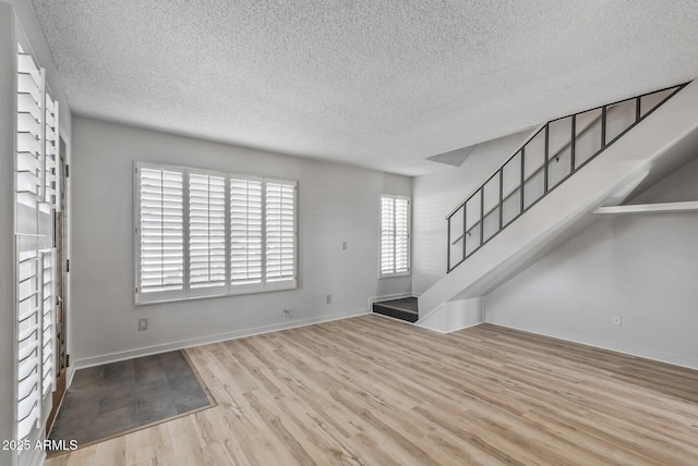 unfurnished living room featuring stairs, wood finished floors, baseboards, and a textured ceiling