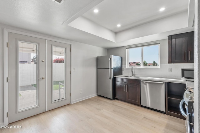 kitchen featuring tasteful backsplash, light wood finished floors, light countertops, stainless steel appliances, and a sink