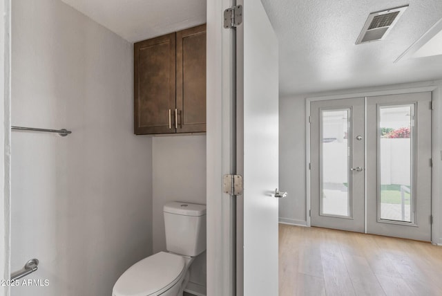 bathroom featuring visible vents, toilet, a textured ceiling, wood finished floors, and french doors