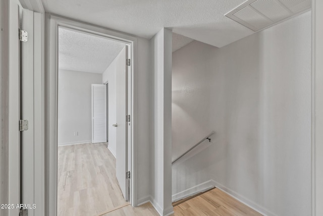 hall featuring visible vents, baseboards, light wood-type flooring, an upstairs landing, and a textured ceiling