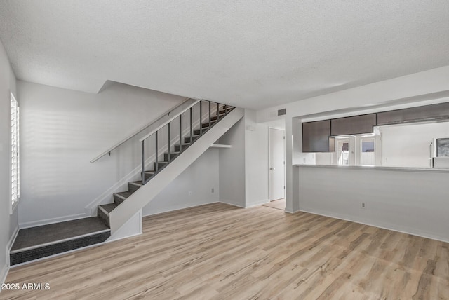 unfurnished living room featuring stairs, wood finished floors, visible vents, and a textured ceiling