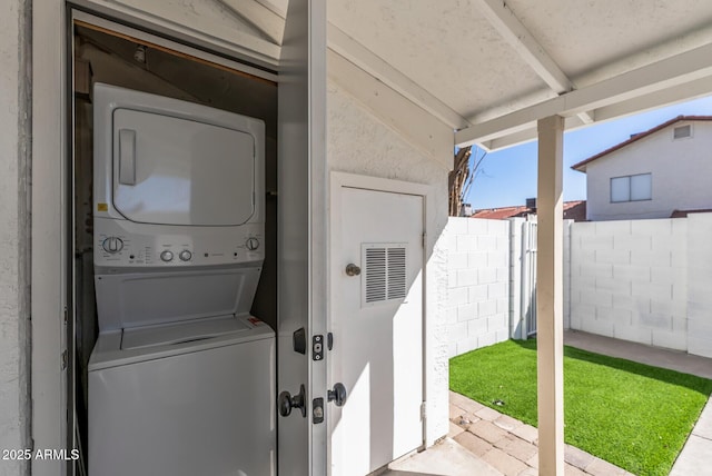 laundry area featuring concrete block wall, laundry area, and stacked washing maching and dryer