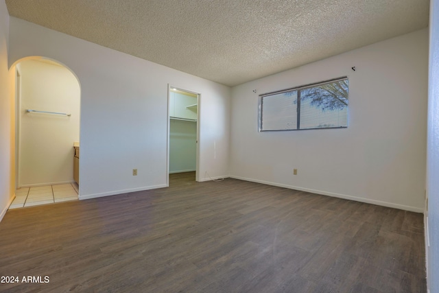 unfurnished bedroom with ensuite bathroom, a spacious closet, a textured ceiling, wood-type flooring, and a closet