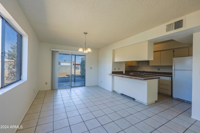 kitchen with kitchen peninsula, a textured ceiling, light tile patterned floors, white refrigerator, and a chandelier