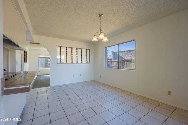 tiled empty room featuring a textured ceiling, a wealth of natural light, and an inviting chandelier