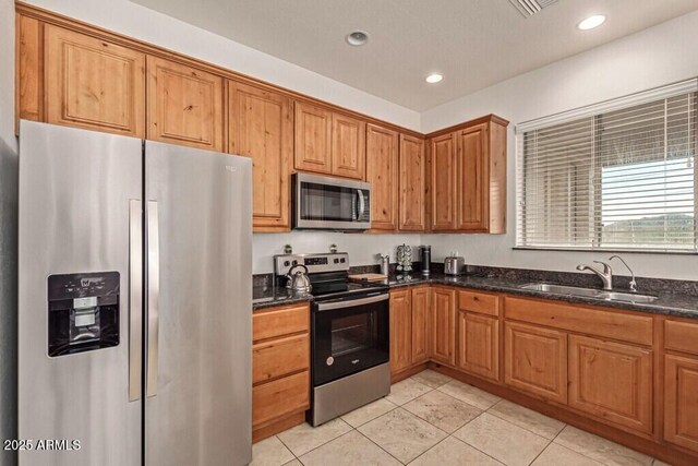 kitchen with a sink, dark stone counters, brown cabinets, light tile patterned floors, and appliances with stainless steel finishes