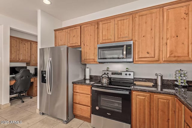 kitchen featuring dark stone counters, light tile patterned floors, stainless steel appliances, and brown cabinets