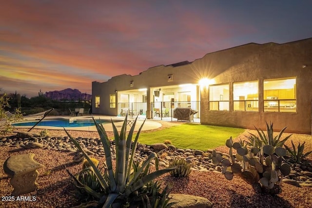 back of property at dusk with stucco siding, a patio, and a fenced in pool