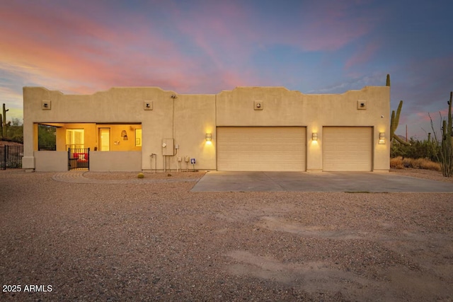 pueblo-style house featuring concrete driveway, an attached garage, stucco siding, and fence