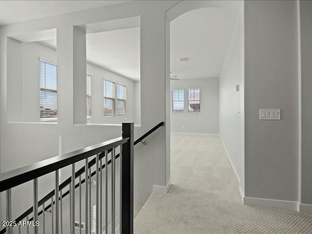 hallway featuring baseboards, visible vents, an upstairs landing, and light colored carpet