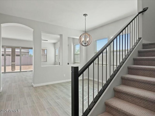 stairs featuring baseboards, a chandelier, and wood finished floors