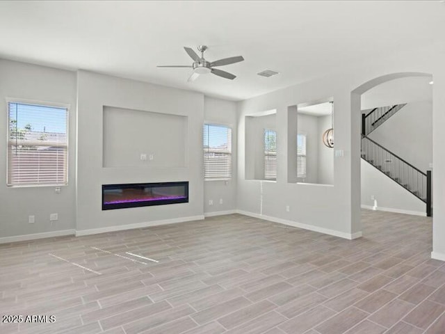 unfurnished living room featuring ceiling fan, stairway, a glass covered fireplace, and light wood-style flooring