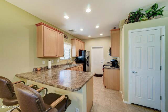 kitchen featuring a kitchen bar, kitchen peninsula, black fridge, and light brown cabinetry