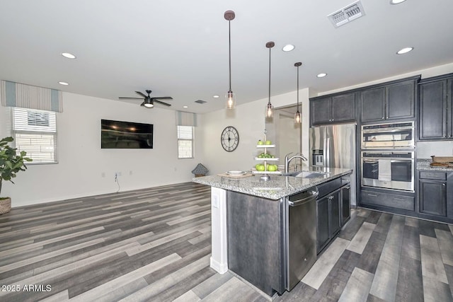 kitchen featuring visible vents, light stone counters, open floor plan, stainless steel appliances, and a sink