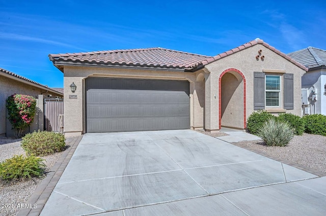 mediterranean / spanish house with a garage, concrete driveway, a tiled roof, and stucco siding