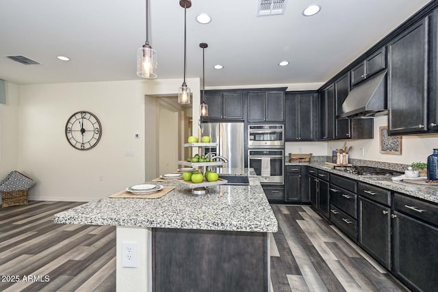 kitchen featuring a center island with sink, visible vents, appliances with stainless steel finishes, dark wood-style flooring, and under cabinet range hood