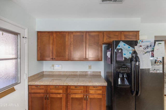 kitchen featuring brown cabinetry, visible vents, tile counters, and black refrigerator with ice dispenser