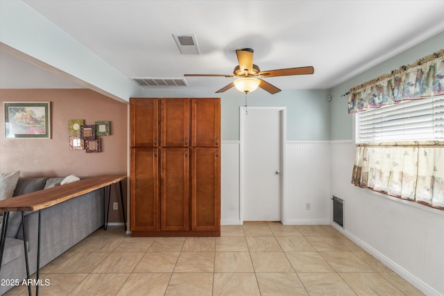 interior space with a wainscoted wall, light tile patterned flooring, a ceiling fan, and visible vents