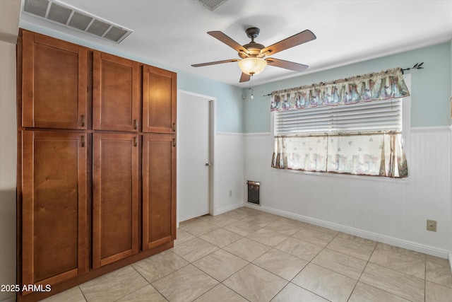 unfurnished bedroom with ceiling fan, light tile patterned floors, visible vents, and wainscoting