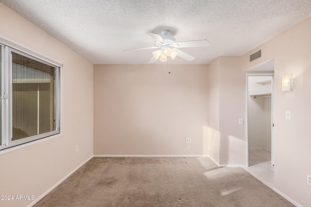 empty room featuring ceiling fan, light colored carpet, and a textured ceiling