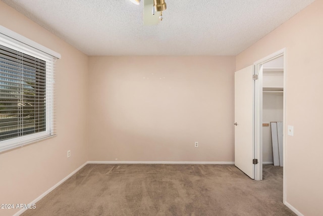 unfurnished bedroom featuring a textured ceiling, a walk in closet, light carpet, and a closet