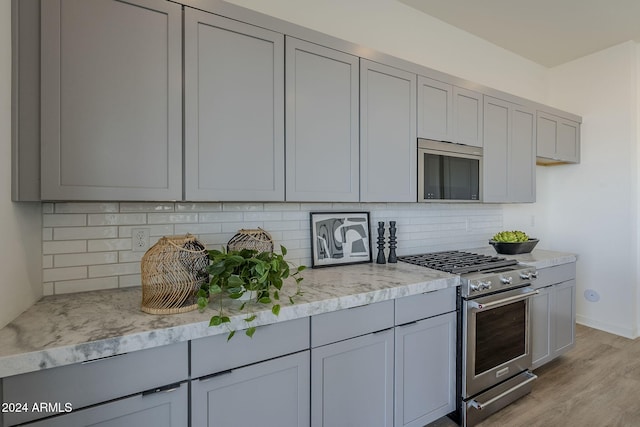 kitchen with appliances with stainless steel finishes, light stone countertops, light hardwood / wood-style flooring, and gray cabinetry