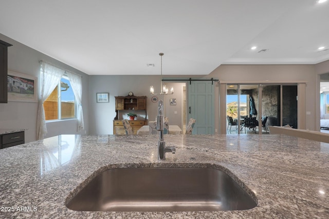 kitchen featuring hanging light fixtures, a barn door, sink, and stone counters