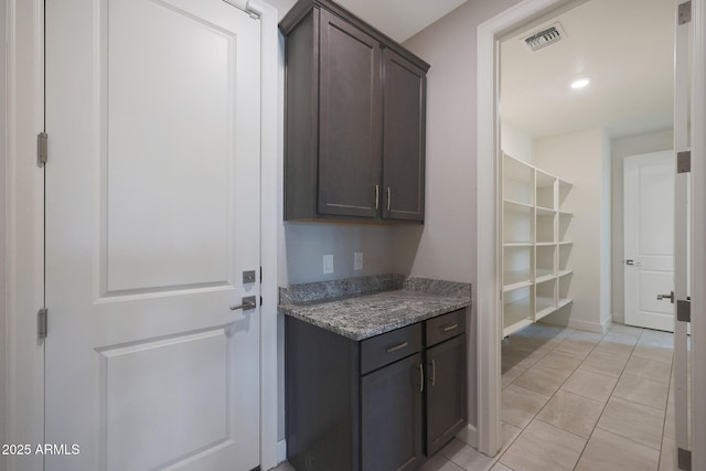 interior space featuring light tile patterned floors, dark brown cabinets, and dark stone countertops