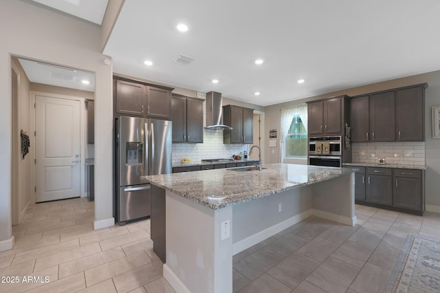 kitchen with appliances with stainless steel finishes, sink, dark brown cabinetry, a center island with sink, and wall chimney exhaust hood