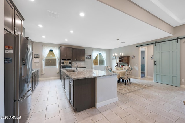 kitchen featuring decorative light fixtures, an island with sink, dark brown cabinetry, stainless steel refrigerator with ice dispenser, and a barn door